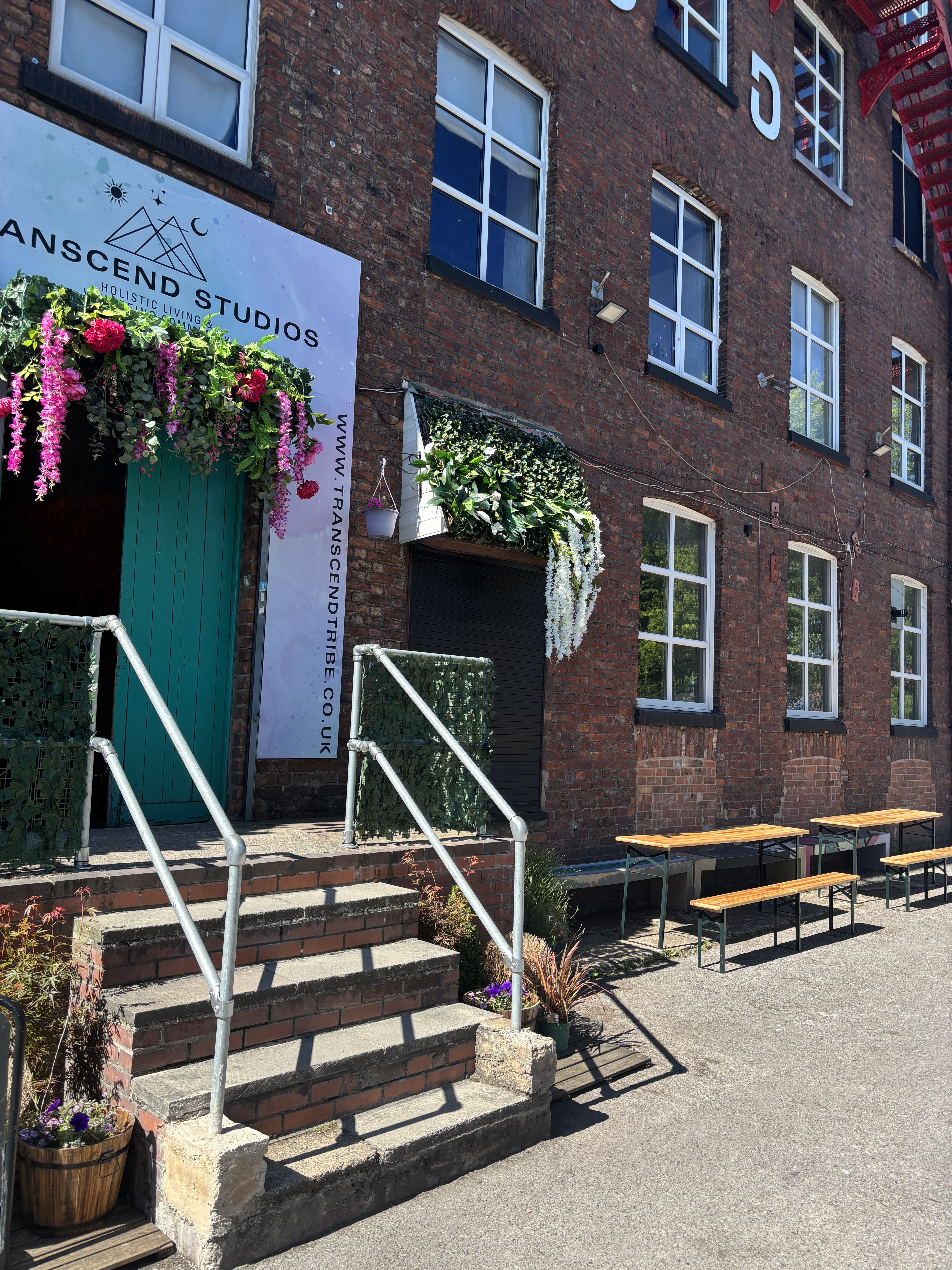 The front of Transcend Studios at Bridgewater Mill, Eccles — flower-covered teal doors, benches outside and free on-site parking